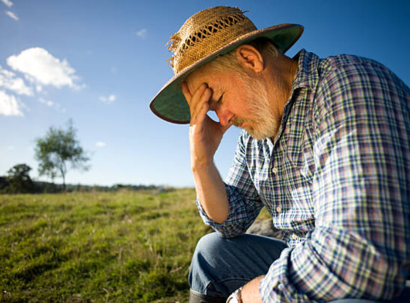 Photograph of a farmer thinking with his head in his hand.